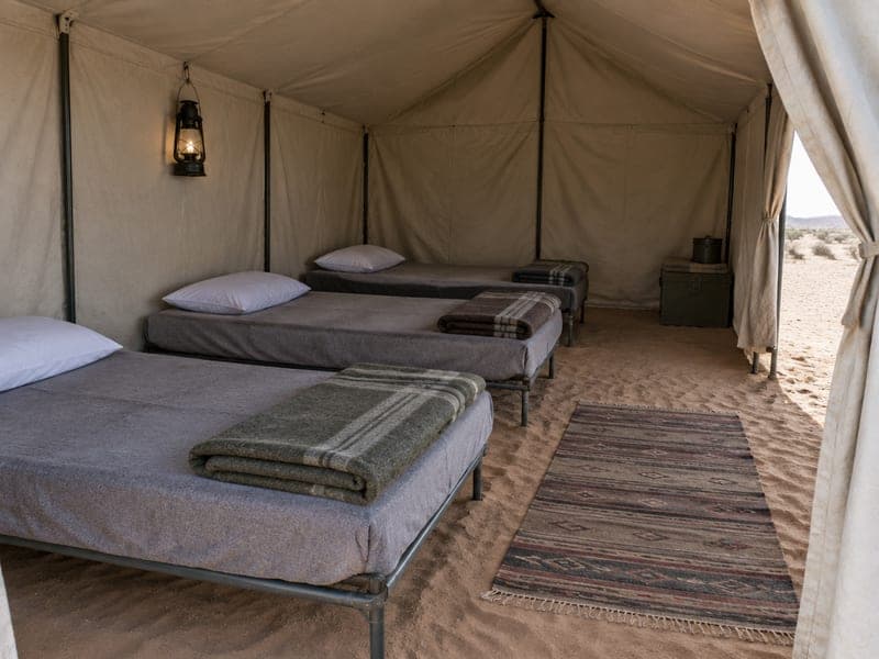 Shared canvas tent with a row of simple camp beds and folded blankets